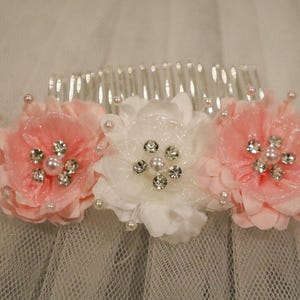 May include: A white hair comb with three pink and white fabric flowers with rhinestone accents.