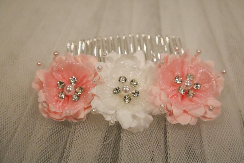 May include: A white hair comb with three pink and white fabric flowers with rhinestone accents.
