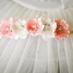 May include: A white tulle fabric with a pink and white flower headband with pearl and rhinestone embellishments.