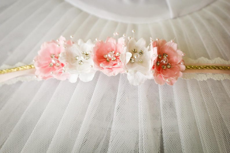 May include: A white tulle fabric with a pink and white flower headband with pearl and rhinestone embellishments.