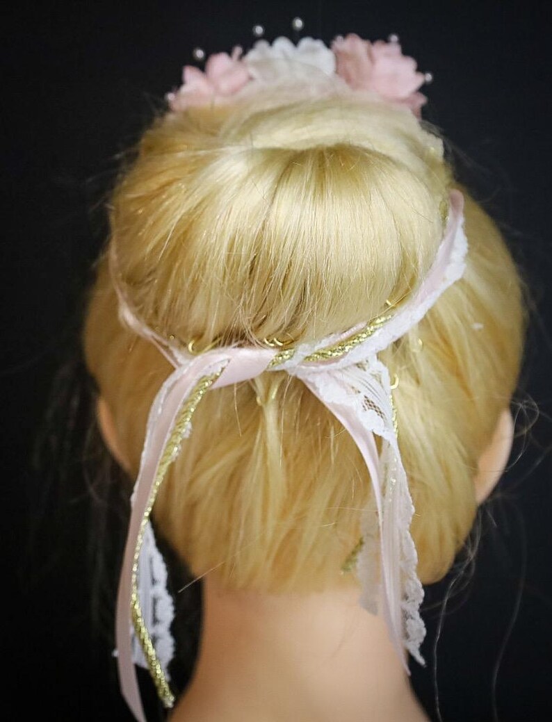 May include: A blonde hair bun with a pink and white flower hair accessory and a pink ribbon with gold trim.