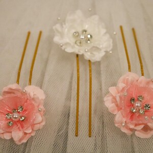 May include: Three gold hair pins with pink and white fabric flowers. Each flower has a pearl and rhinestone embellishment in the center.