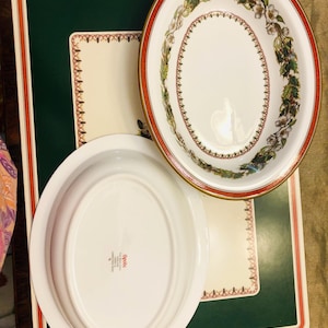 May include: Two white oval ceramic serving dishes with a green and red floral design. The larger dish has a gold rim and the smaller dish has the text "Pfaltzgraff" on the bottom.
