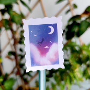 May include: A decorative stamp-shaped sticker featuring a dreamy night sky scene. The design includes a crescent moon, stars, and a silhouette of a creature against a backdrop of purple and blue hues. The sticker has a white, scalloped border.