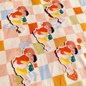 Puede incluir: Cinco pegatinas coloridas con parejas de dibujos animados que sostienen cubos. Las pegatinas est&aacute;n sobre un fondo a cuadros rosa y naranja.