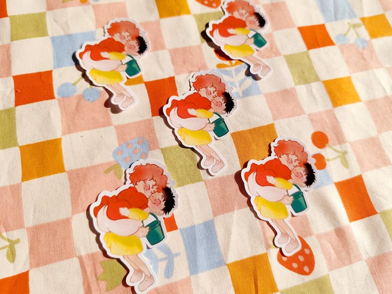 Puede incluir: Cinco pegatinas coloridas con parejas de dibujos animados que sostienen cubos. Las pegatinas est&aacute;n sobre un fondo a cuadros rosa y naranja.