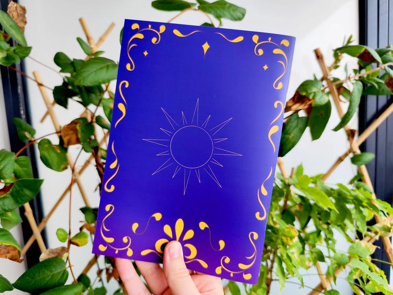 May include: A blue card with a sun design and gold decorative accents. The sun is in the center, with a starburst pattern. The card has gold floral and swirl designs around the edges.