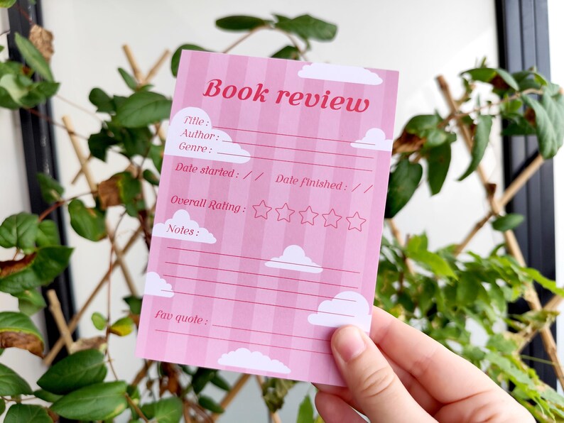 May include: A pink book review card with a striped background and cloud illustrations. The card includes fields for title, author, genre, dates, rating, notes, and a favorite quote. The text "Book review" is at the top.