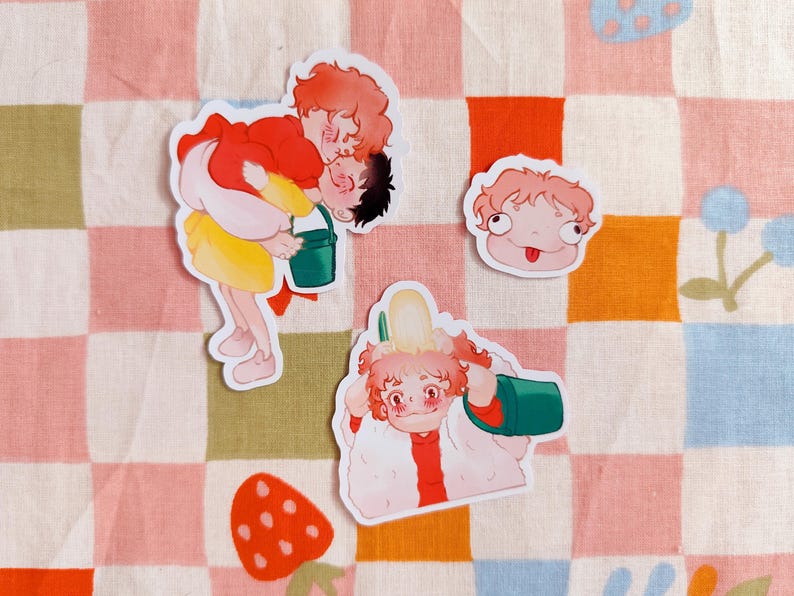 Puede incluir: Tres pegatinas de personajes de dibujos animados sobre un fondo de cuadros rosa y blanco. Las pegatinas muestran a una ni&ntilde;a llevando a un ni&ntilde;o, una ni&ntilde;a con un cubo y una ni&ntilde;a con la lengua fuera.