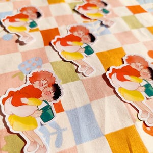 Puede incluir: Cuatro pegatinas coloridas con parejas de dibujos animados que sostienen cubos. Las pegatinas est&aacute;n sobre un fondo a cuadros.