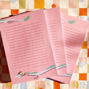 Op de afbeelding: Drie roze notitieblokken met gestreept papier en een groene en witte illustratie van een draak op elke pagina.