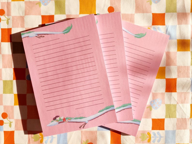 Op de afbeelding: Drie roze notitieblokken met gestreept papier en een groene en witte illustratie van een draak op elke pagina.