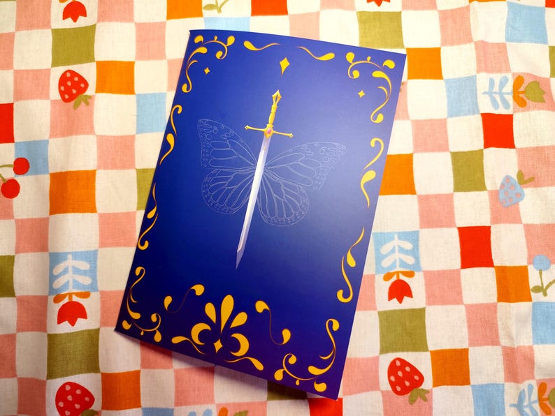 May include: A blue book cover with a gold sword design and a butterfly outline. The cover has gold decorative flourishes and is set against a colorful checkered background with strawberries and flowers.