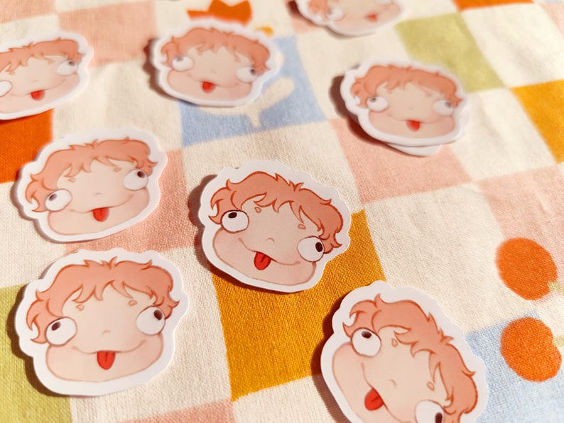 Puede incluir: Un conjunto de ocho pegatinas de personajes de dibujos animados con fondo blanco y detalles en rosa y rojo. Los personajes tienen ojos grandes y sacan la lengua. Las pegatinas est&aacute;n sobre un fondo a cuadros.