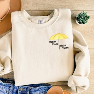 May include: A cream-colored sweatshirt with a yellow umbrella graphic and the text "Right Place Right Time".
