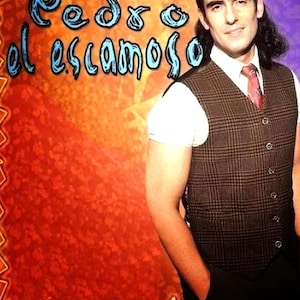May include: A man with a brown vest and a red tie stands in front of a colorful background. The text "Pedro el Escamoso" is written in blue letters on the background.