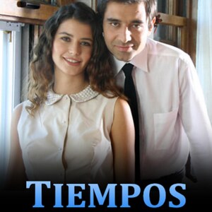 May include: A couple poses for a photo in front of a window. The woman is wearing a white collared shirt with a pearl necklace. The man is wearing a white shirt and a black tie. The text "TIEMPOS PASADOS" is displayed in blue letters on a black background.