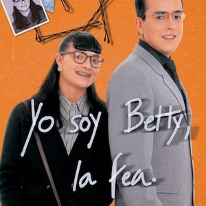 May include: A poster for the Colombian telenovela "Yo soy Betty, la fea" featuring two actors. The woman is wearing glasses and braces and has dark hair. The man is wearing a gray suit and a black tie. The text on the poster reads "Yo soy Betty, la fea".
