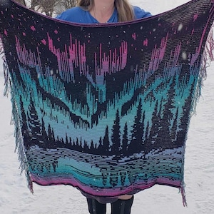 May include: A crocheted blanket with a black background and a colorful aurora borealis design. The blanket has fringe on all sides.