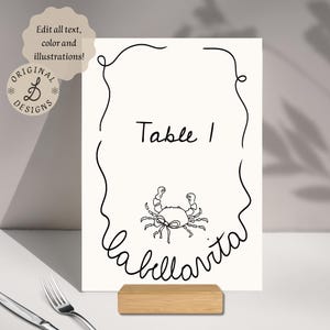May include: Black and white table number card with a crab illustration and the text "Table 1" and "la ballarita".