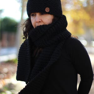 May include: A black knit hat and scarf set. The hat has a small, round, brown button on the side. The scarf is long and thick, and the set appears to be made of a soft, warm material. The set is perfect for cold weather.