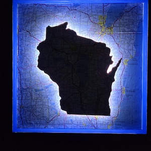 Puede incluir: Un mapa enmarcado de Wisconsin con una silueta del estado recortada e iluminada con luz azul.