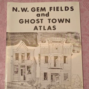 May include: A book cover titled "N.W. Gem Fields and Ghost Town Atlas." The cover features a black and white illustration of two old buildings, possibly in a ghost town. The words "8th Edition" are at the bottom.