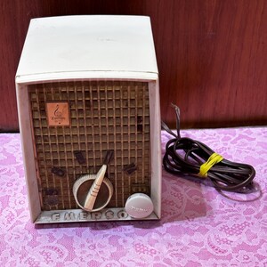 May include: Vintage Emerson radio with a cream-colored cabinet and a brown speaker grill. The radio features a tuning dial and control knobs. The word "Emerson" is printed on the front. A brown power cord is attached.