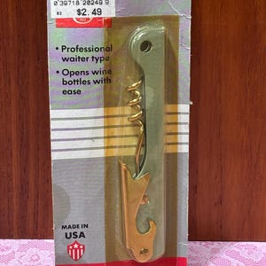 May include: A vintage corkscrew in its original packaging. The packaging is green, gold, and red, with the words "Corkscrew" and "Made in USA." The corkscrew is a professional waiter type and opens wine bottles with ease.