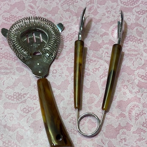 May include: A vintage bar set featuring a cocktail strainer with a coiled spring, and a pair of ice tongs. The handles have a brown, marbled appearance. The set is made of stainless steel and is designed for mixing drinks.