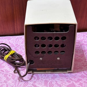May include: A vintage Emerson Radio & Phonograph, cream-colored with a dark brown speaker panel. The back panel has multiple circular openings and text that reads "Emerson Radio & Phonograph Corporation New York U.S.A."