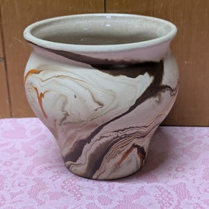 May include: A white ceramic vase with brown and orange marbling. The vase has a rounded body and a wide opening.