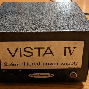 May include: A black Vista IV Deluxe filtered power supply with an on/off switch and a red button. The power supply is made in the USA and has a label that says "Clifford Industries, Inc."