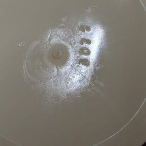 May include: Close-up of a light beige plastic object with the number "4073" printed on it. The object has a circular indentation in the center and a textured surface with cracks radiating outwards.