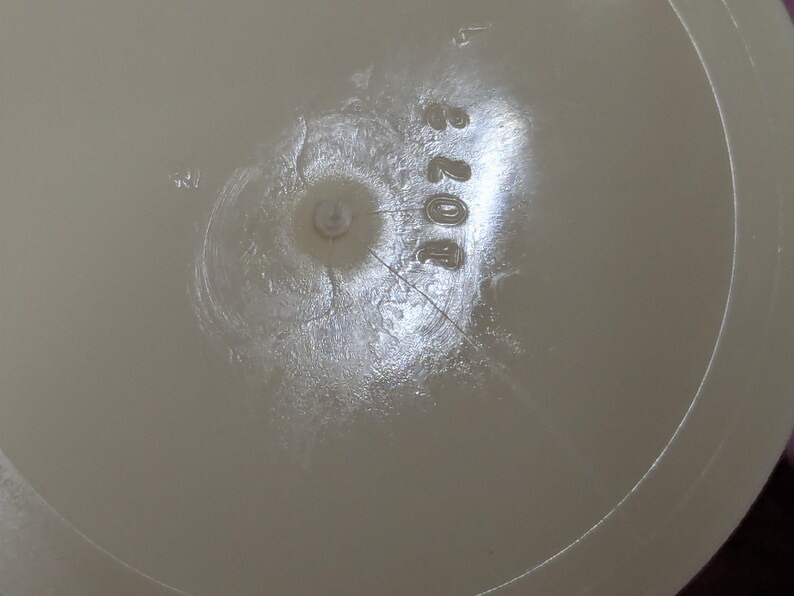 May include: Close-up of a light beige plastic object with the number "4073" printed on it. The object has a circular indentation in the center and a textured surface with cracks radiating outwards.