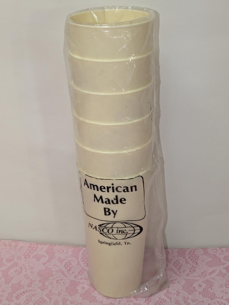 May include: A stack of six off-white, cylindrical cups wrapped in clear plastic. The cups have a ridged design. The packaging includes the text "American Made By NASCO inc. Springfield, Tn."