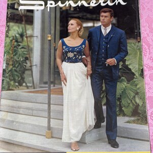 May include: Vintage magazine cover featuring a woman in a blue and white dress and a man in a blue suit. The magazine title is "Spinnerin" with the tagline "Serenely Stimulating". The cover has a retro aesthetic.