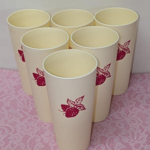 May include: Set of seven cream-colored tall plastic tumblers. Each tumbler features a red strawberry design. The tumblers are arranged in a semi-circular pattern, showcasing their uniform shape and design. Ideal for serving cold beverages.