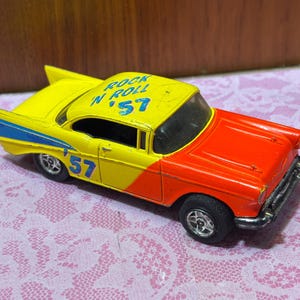 May include: A vintage toy car in yellow and red, with the text "Rock 'n Roll '57" on the roof. The car has black wheels and the number "57" on the side. The car is a classic model.