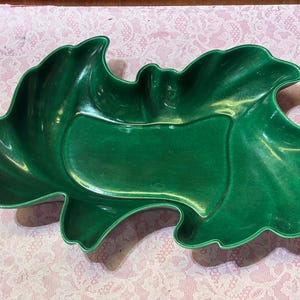 May include: A glossy, emerald green ceramic serving dish. The dish is shaped like a stylized leaf with a central rectangular section. The edges of the dish have a wavy, scalloped design.