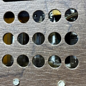 May include: Close-up of a vintage radio component with a brown, textured surface. The component features multiple circular openings revealing internal parts. Text at the bottom instructs on tube replacement. Two screws are visible.