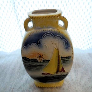 May include: A small, yellow and blue ceramic vase with a painted scene of a sailboat and a windmill. The vase has two handles and a rounded oval shape.