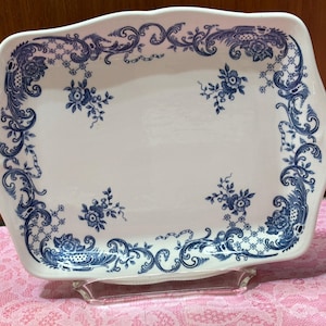 May include: A rectangular white ceramic tray with scalloped edges, featuring a blue floral pattern along the border and small floral sprigs in the center. The design includes intricate scrollwork and lattice details in a classic blue and white color scheme.