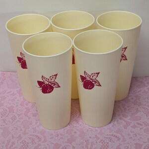 May include: Five tall, cream-colored plastic tumblers with a red strawberry and leaf design. The tumblers have a simple, cylindrical shape and a white rim. The design is repeated on each tumbler.