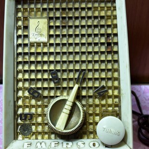 May include: Vintage Emerson radio with a cream-colored plastic frame and a gold-toned metal speaker grill. Features a tuning dial, volume controls, and the Emerson logo. The word "TUNING" is printed on the tuning knob.