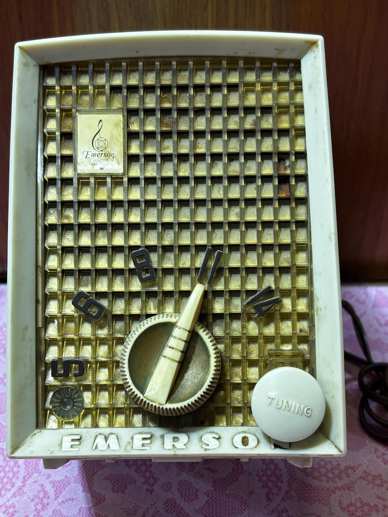May include: Vintage Emerson radio with a cream-colored plastic frame and a gold-toned metal speaker grill. Features a tuning dial, volume controls, and the Emerson logo. The word "TUNING" is printed on the tuning knob.