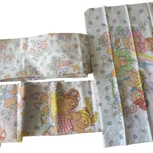 May include: White Cabbage Patch Kids bedding set with floral and character prints. The set includes a flat sheet, fitted sheet, and pillowcases. The sheets feature a repeating pattern of flowers and Cabbage Patch Kids characters in various poses.