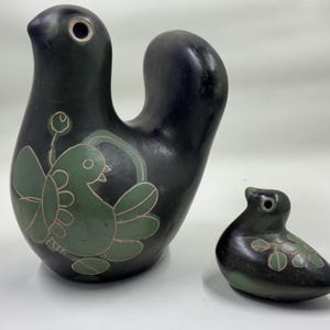 May include: Two dark green ceramic bird ornaments. The larger bird has a curved neck and a green bird design with a white outline. The smaller bird is a solid dark green with a green leaf design.