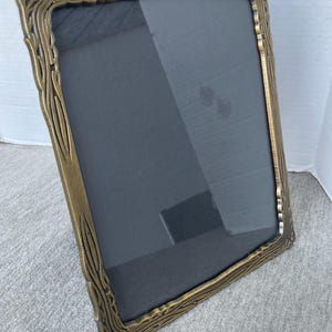Peut inclure: Un cadre photo rectangulaire de style antique avec une finition bronze. Le cadre a une bordure détaillée et texturée avec un motif en forme de bois. Le cadre contient une surface sombre et réfléchissante, probablement en verre ou en acrylique.