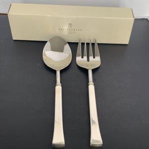 May include: A silver serving set with a spoon and fork in a Pottery Barn box. The set is made of polished stainless steel with square handles.